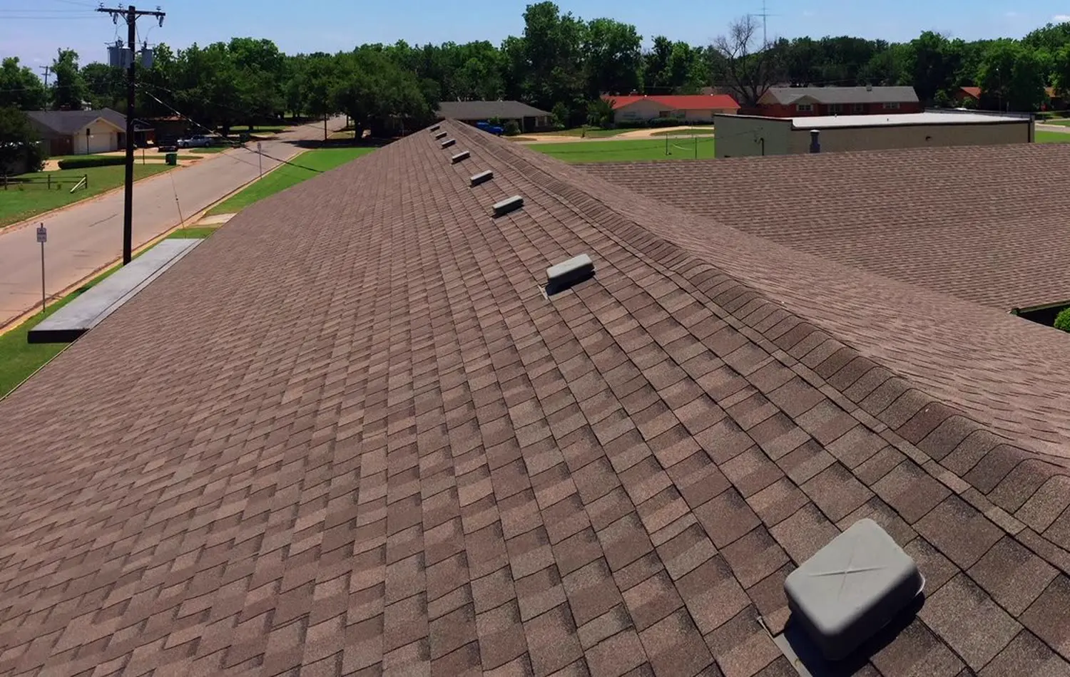 Sample after photo: a long low roof seen from above, covered in new brown shingles, with a quiet street beside it.