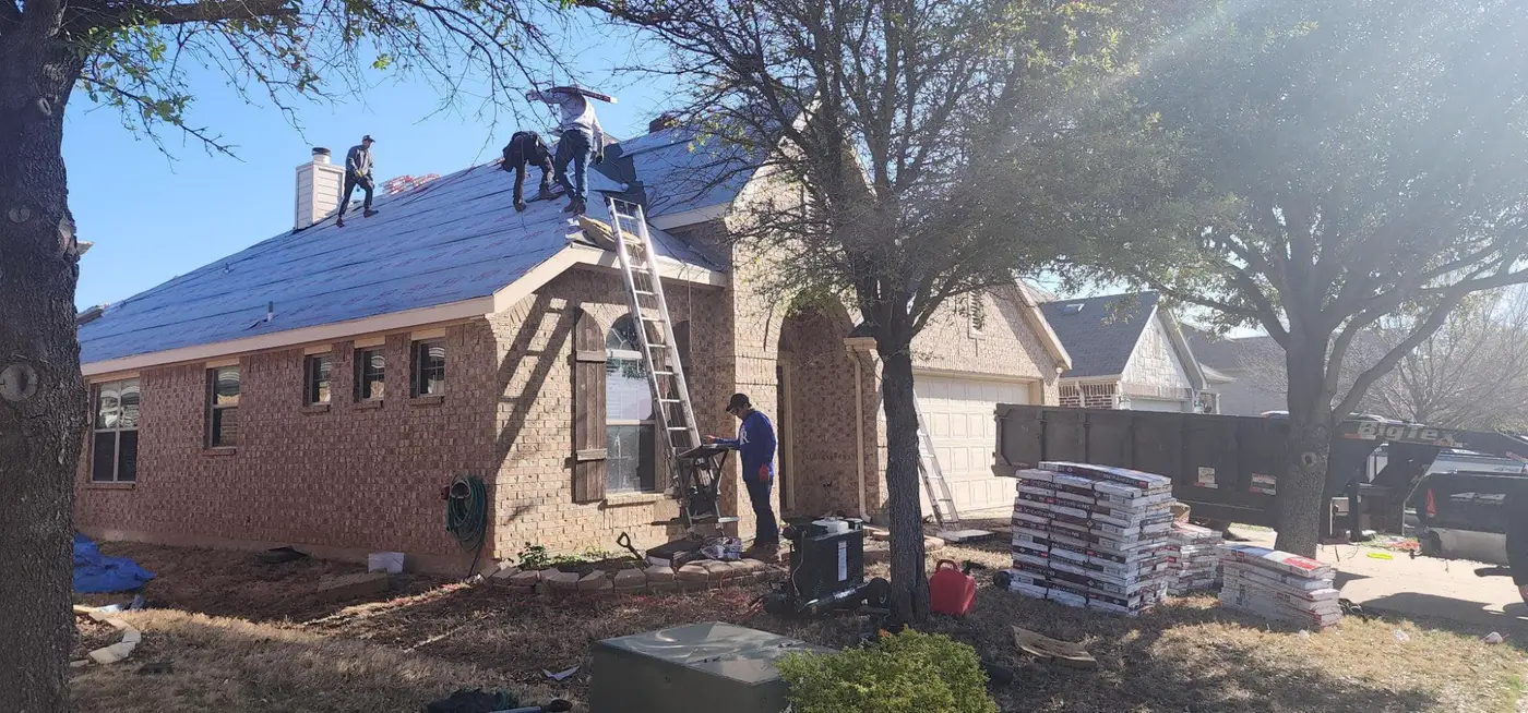 The Mataska crew on a brick house roof laying underlayment, with bundles of new shingles stacked in the yard.