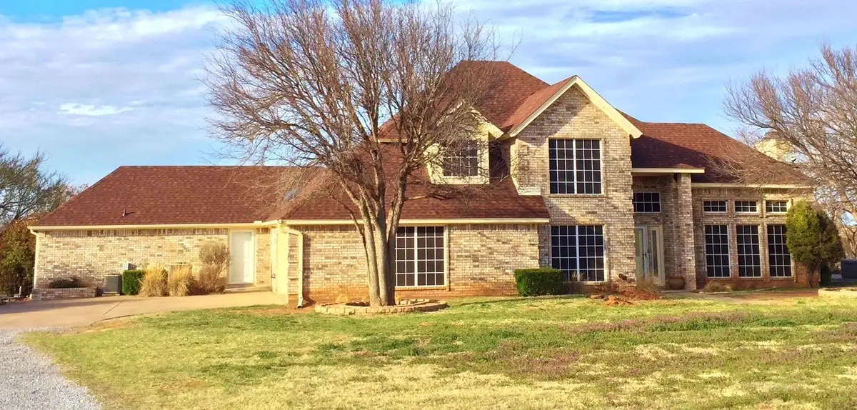 A large stone ranch house with a new red-brown shingle roof under a big Texas sky.