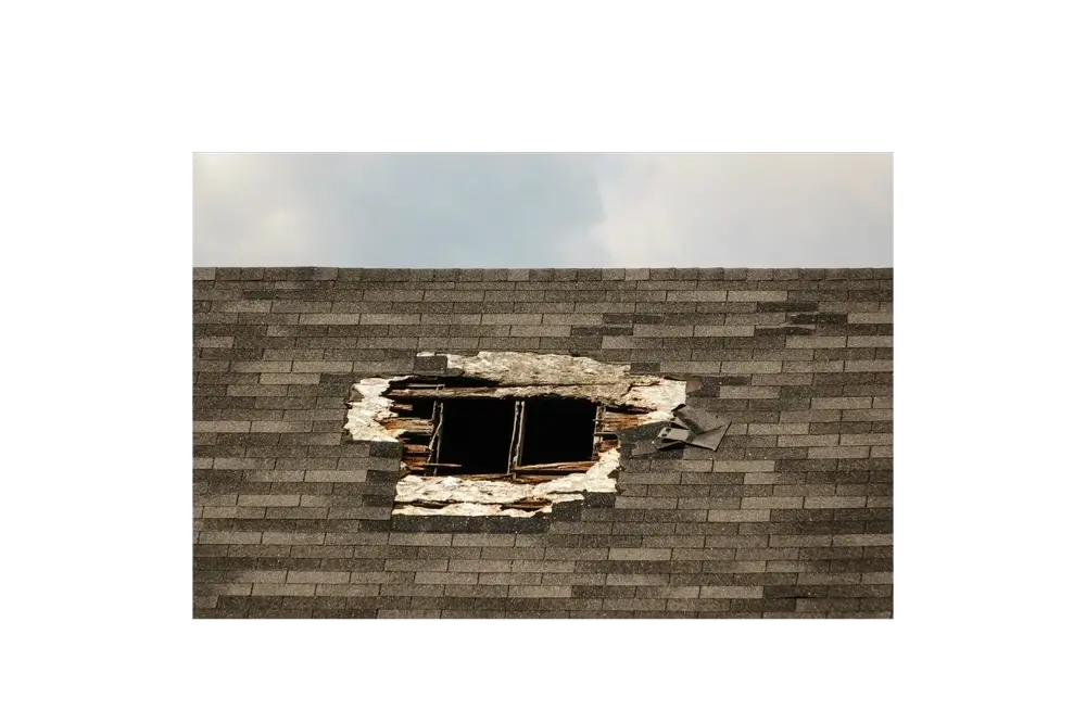 A hole torn through old grey shingles, showing the wood deck underneath.