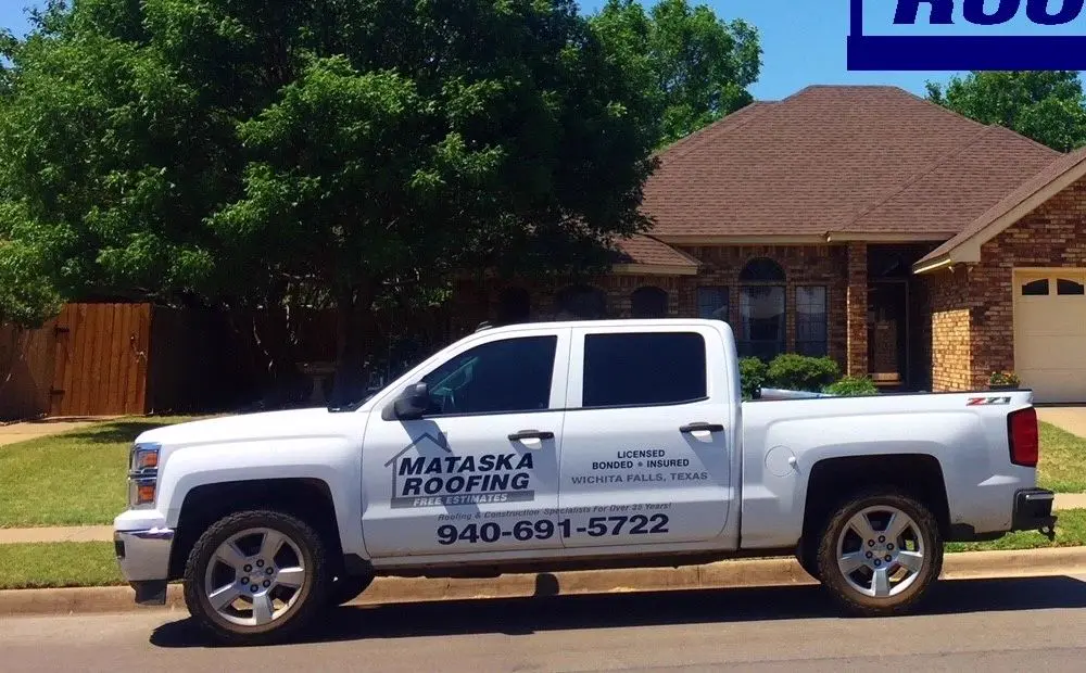 A white Mataska Roofing pickup truck with the phone number on the door, parked outside a brick house.
