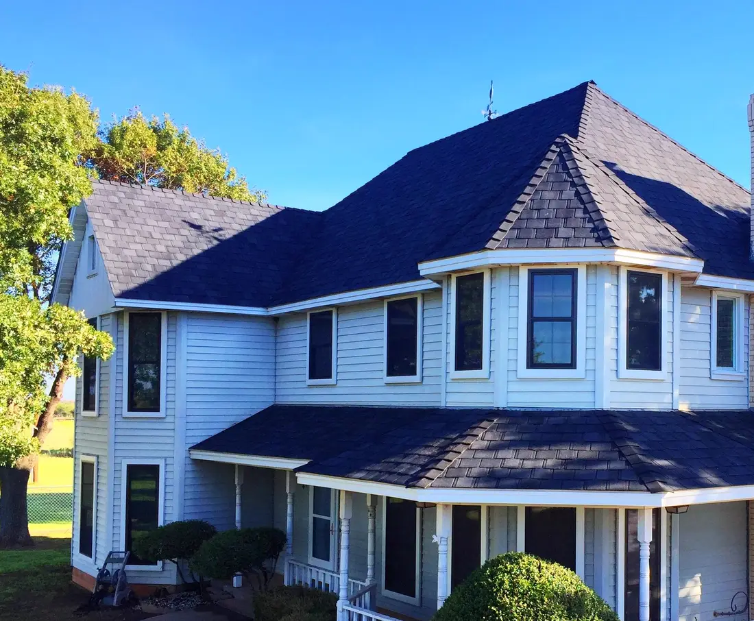 A two-story white Victorian house with a wraparound porch and a new dark shingle roof by Mataska Roofing.
